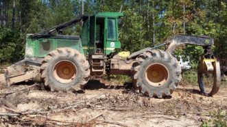 A four-wheeled grapple skidder with a large grapple touching the ground is parked with a view of its side.