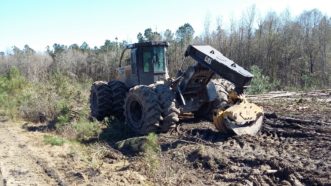 A four-wheeled grapple skidder with dual tires is parked with a closed grapple on the ground.