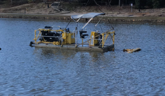 A photo shows equipment for hydraulic dredging onboard a small pontoon boat floating on a pond. 